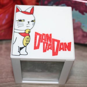 May include: White photo frame with a red and white cartoon cat and the text "DAN DADAN" in red glitter. The frame has a clear window to insert a photo.