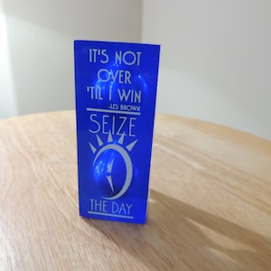 May include: Blue acrylic block with the text "It's not over til I win -Les Brown SEIZE THE DAY" in white lettering.