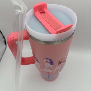 May include: A pink insulated tumbler with a handle and a lid featuring a pink flip-top closure. The tumbler has a silver rim and a design of cartoon figures. A clear plastic straw is included.