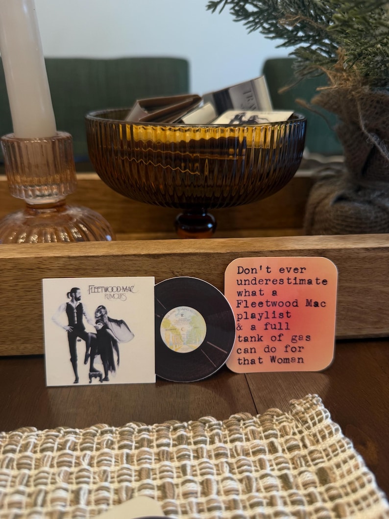 May include: A collection of Fleetwood Mac themed items. Includes a square album cover print, a vinyl record, and a coaster with text that reads "Don't ever underestimate what a Fleetwood Mac playlist & a full tank of gas can do for that Woman."