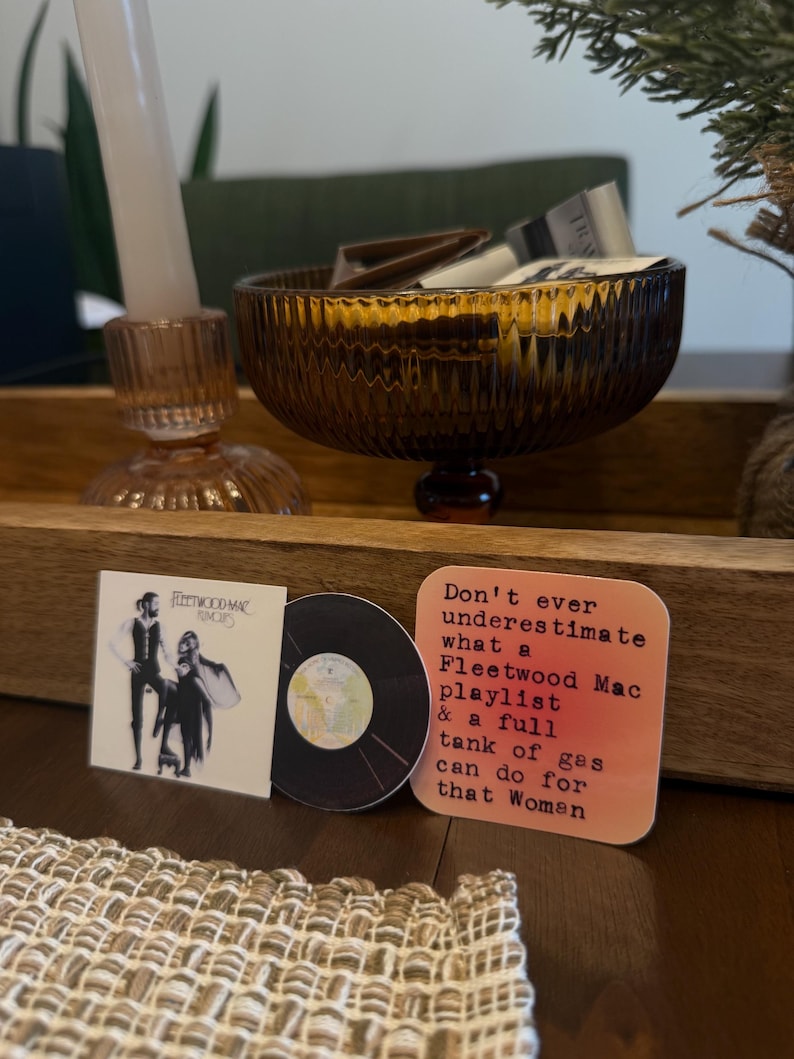 May include: A decorative wooden tray holds a brown glass bowl, a pink candle holder with a white candle, and two coasters. One coaster features a Fleetwood Mac album cover, and the other reads, "Don't ever underestimate what a Fleetwood Mac playlist & a full tank of gas can do for that Woman."