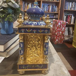 May include: A gold and blue cloisonn&eacute; clock with intricate floral designs. The clock has a domed top and stands on a base with four legs.
