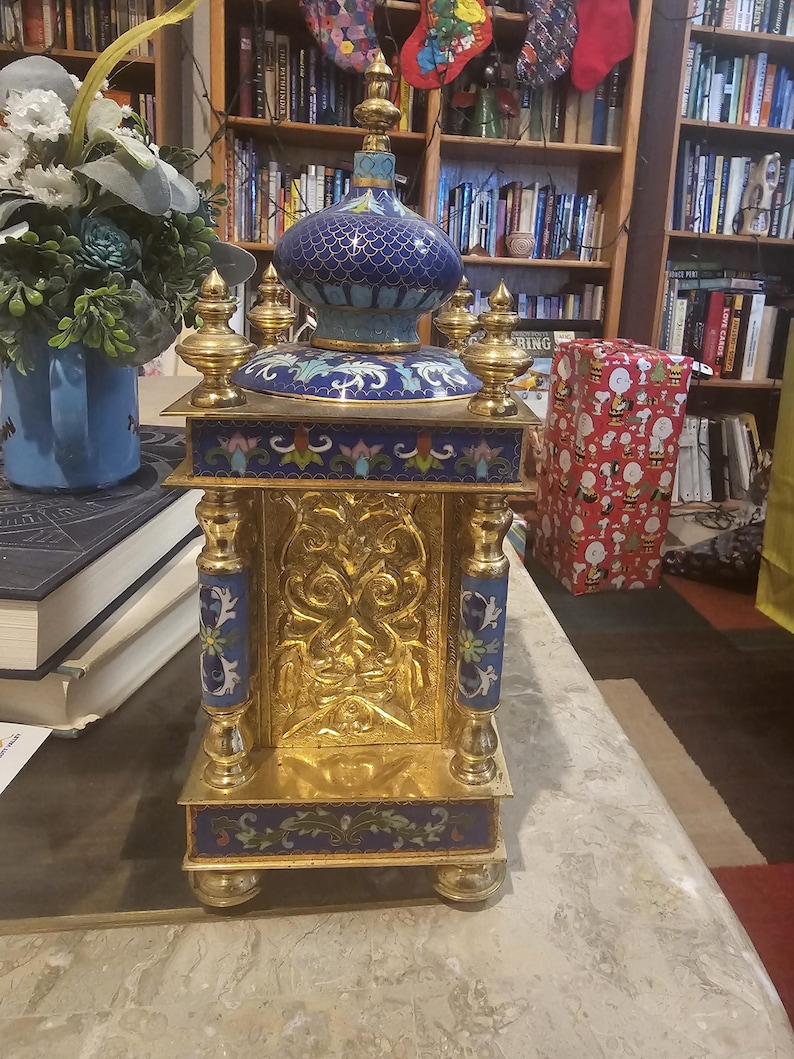 May include: A gold and blue cloisonn&eacute; clock with intricate floral designs. The clock has a domed top and stands on a base with four legs.