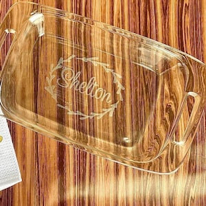 May include: A white kitchen towel with the text "The Sheltons" and a design of kitchen utensils. A clear glass baking dish with the text "Shelton" etched into it.