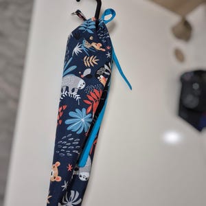 May include: A blue fabric storage bag with a hanging loop and a blue ribbon. The bag has a jungle animal print with sloths, monkeys, and leaves.