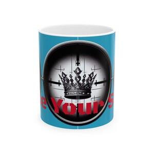 May include: A white ceramic mug with a light blue exterior. The mug features a black and white graphic of a crown inside a scope, with the red text "Be Yours" wrapping around the bottom of the scope.