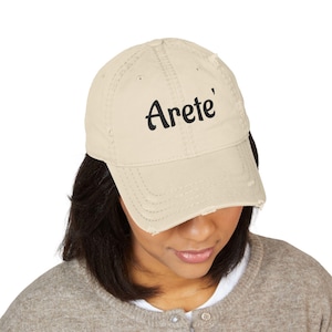 May include: A distressed, cream-colored baseball cap with the word "Arete'" printed in black. The cap has a curved brim and a worn appearance, suggesting a vintage or casual style. The cap is a classic six-panel design.