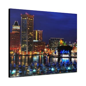 May include: A canvas print of a nighttime cityscape featuring illuminated skyscrapers and a harbor filled with boats. The buildings are lit with warm orange and yellow lights, reflecting in the water under a deep blue sky. The overall theme is urban and scenic.