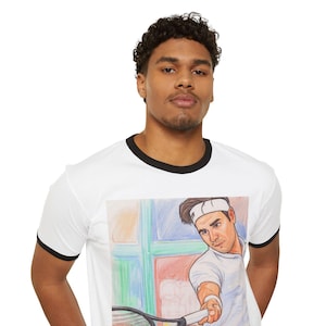 Peut inclure: T-shirt blanc à col et manches noirs. Il présente une illustration colorée d'un joueur de tennis en action, tenant une raquette. L'œuvre est placée devant une fenêtre aux carreaux colorés.