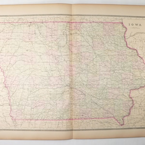 May include: A vintage map of Iowa, printed in black and white with pink and green accents. The map shows the state's counties, cities, and major roads. The title "IOWA" is printed in the upper right corner.