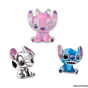 May include: Three character charms in the image. One is pink with purple accents, one is silver, and the last is blue with teal accents. All three charms have large ears and are in a sitting position. The charms are likely for a bracelet or necklace.