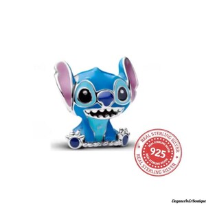 May include: A blue and silver charm featuring the character Stitch from the Disney movie Lilo & Stitch. The charm has large black eyes, a wide grin, and large ears with pink accents. The charm is marked with a "Real Sterling Silver 925" stamp.