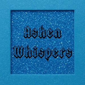May include: A square of sparkling blue glitter with the words "Ashen Whispers" in a gothic font. The glitter square is set within a solid blue frame, creating a contrasting visual effect.