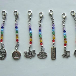 May include: Seven beaded charms with silver-tone clasps and pendants. Each charm features a rainbow gradient of colorful beads. The pendants include an Om symbol, a Buddha, lotus flowers, the word "Namaste", a yoga heart, and a Hamsa hand.