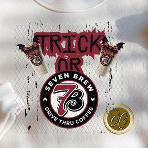 Könnte beinhalten: Cremefarbenes Sweatshirt mit dem Schriftzug "Trick or Seven Brew Drive Thru Coffee" in einem Used-Design. Das Design umfasst Kaffeetassen und eine goldfarbene Münze. Das Sweatshirt ist aus weichem Material.