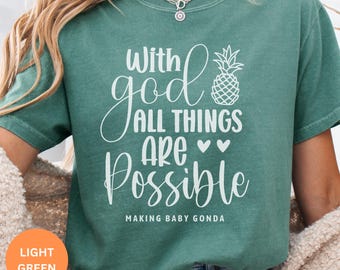 Puede incluir: Camiseta verde claro con el texto blanco "With God All Things Are Possible" y un dibujo de piña. La frase "MAKING BABY GONDA" está impresa debajo. La camiseta es de color liso.
