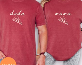 May include: Two crimson short-sleeve t-shirts. The left shirt features the white text "dada" above a white pizza slice graphic. The right shirt features the white text "mama" above a white pizza slice graphic. Both shirts have a crew neckline.