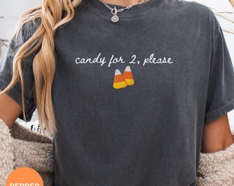 May include: A charcoal gray short-sleeve t-shirt featuring the white text "candy for 2, please" printed above a graphic of two pieces of orange, yellow, and white candy corn. The shirt has a crew neckline and a relaxed, vintage-washed appearance.