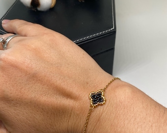 Puede incluir: Un brazalete de cadena dorada con un dije de trébol de cuentas negras.