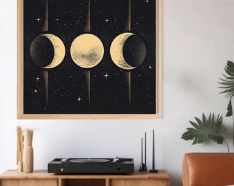 May include: A framed print featuring a celestial design with three moon phases in shades of gold against a black starry background. The artwork is displayed above a wooden cabinet with a record player and decorative items, creating a stylish interior scene.