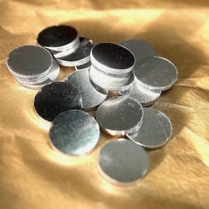 May include: A pile of silver-colored metal discs, some stacked on top of each other, on a brown paper surface.