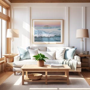 May include: A living room with a light-colored sofa, throw pillows, and a wooden coffee table. A framed picture of a seascape hangs above the sofa. Two lamps with beige shades flank the sofa. A potted plant and a woven basket add decorative touches.