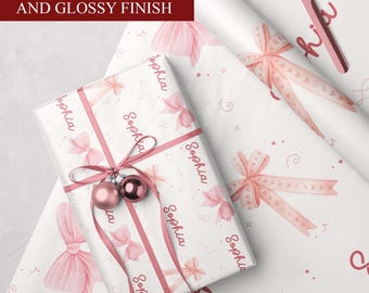 May include: White wrapping paper with a pink bow and ribbon design, with the name "Sophia" printed repeatedly. A wrapped gift with pink ornaments and ribbon is on top. The text "AVAILABLE IN MATTE AND GLOSSY FINISH" is in a maroon box.