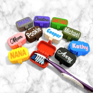 May include: A collection of personalized toothbrush cases in various colors, each with a name printed on the lid. One case is open, revealing a toothbrush. The cases are in shades of gray, purple, green, pink, brown, white, black, and blue.