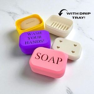May include: A collection of colorful soap containers, including yellow, purple, and pink. The pink container has the word "SOAP" cut out. The purple container has the words "WASH YOUR HANDS!" cut out. One container is white with a drip tray, and another is white with heart cutouts.