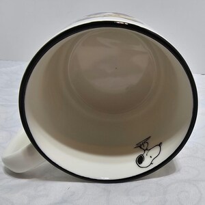 Pu&ograve; includere: Tazza in ceramica bianca con bordo e manico neri. L'interno presenta un'illustrazione a cartoni animati di Snoopy con cappello e occhiali da aviatore. La tazza &egrave; progettata per bevande calde e ha un design classico.