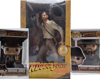 Può includere: Tre oggetti da collezione di Indiana Jones: una statua in vinile da 25 cm e due figure Pop!. La statua raffigura Indiana Jones con una camicia beige e pantaloni marroni. Le figure Pop! sono in scatole, una con la scritta "Indiana Jones" e l'altra "Henry Jones Sr."