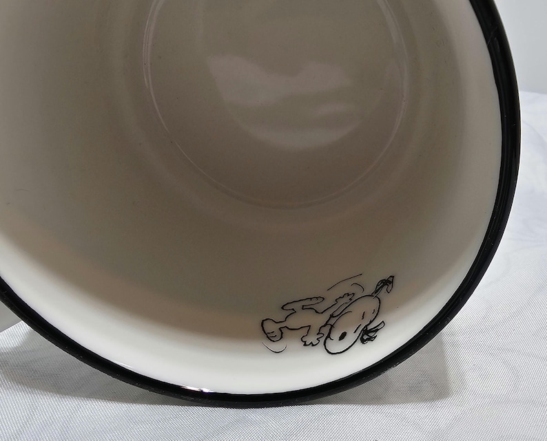 Pu&ograve; includere: Una ciotola di ceramica bianca con bordo nero. Un'illustrazione a cartoni animati in bianco e nero di Snoopy &egrave; sul lato della ciotola. La ciotola &egrave; vuota e sembra pulita.