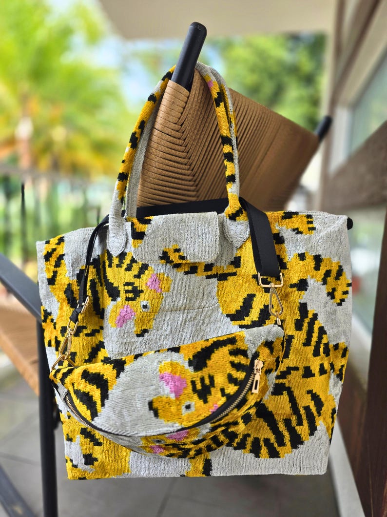 May include: A tote bag and a matching fanny pack featuring a yellow, black, and gray tiger stripe pattern with pink accents. Both items have a textured, velvet-like surface, black fabric straps, and gold-toned metal hardware clips and zippers.