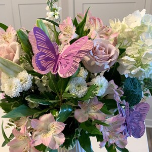以下が含まれることがあります： 白い花瓶にピンクと白の花束と紫色の紙の蝶々