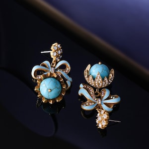 May include: A pair of gold-toned earrings with turquoise-colored orbs and light blue enamel bow accents. The earrings feature small, sparkling crystal embellishments and a post-back closure.