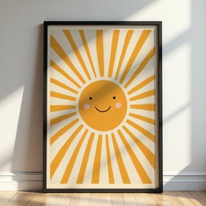 以下が含まれることがあります： 中央に黄色い太陽が描かれた額装アートプリント。太陽にはシンプルな黒い線の笑顔、2つの黒い点の目、2つの小さなピンクの丸い頬がある。太陽からは黄色い光線が放射状に伸びており、背景はクリーム色である。