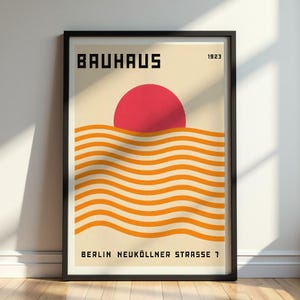 May include: Framed Bauhaus art print featuring a red sun over orange wavy lines, with the word "BAUHAUS" in bold black letters at the top and "BERLIN NEUKÖLLNER STRASSE 7" at the bottom. The year "1923" is also displayed.