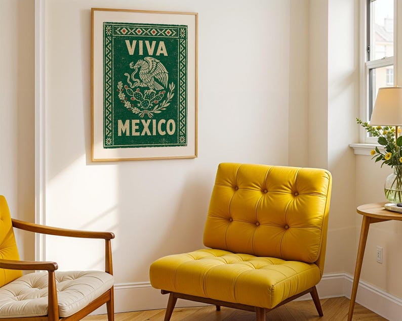 A framed green print with a distressed texture, featuring a white eagle on a cactus with a snake in its beak, and the words "VIVA MEXICO" above and below, hangs on a white wall above a yellow armchair in a living room setting.