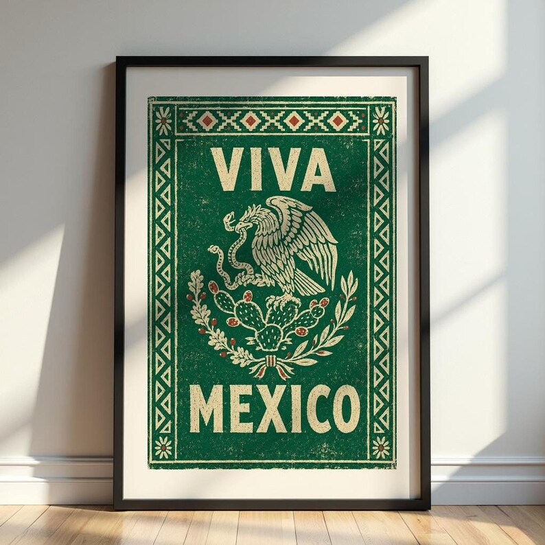 A framed green print with a distressed texture, featuring a white eagle on a cactus with a snake in its beak, and the words "VIVA MEXICO" above and below, leans against a white wall on a dark wood floor.