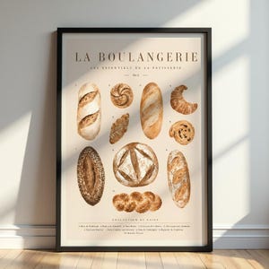 May include: A framed print featuring watercolor illustrations of various breads and pastries. The print includes a baguette, croissant, and other baked goods. Text at the top reads "LA BOULANGERIE" and "LES ESSENTIALS DE LA PATISSERIE". The print is in a black frame.