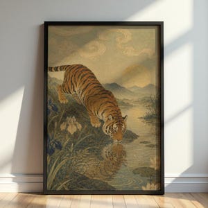 May include: Framed art print featuring a tiger drinking from a body of water. The tiger has orange and black stripes. The artwork has a vintage aesthetic, with a landscape of mountains, water lilies, and irises. The frame is black.