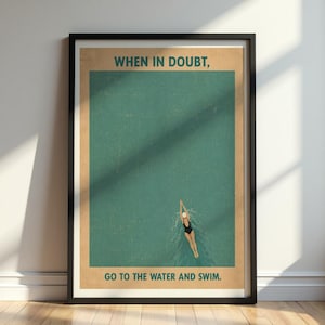 Op de afbeelding: Een ingelijste kunstdruk met een blauwgroene waterachtergrond en een zwemmer in een zwart badpak en witte badmuts. De tekst bovenaan luidt "WHEN IN DOUBT," en de tekst onderaan "GO TO THE WATER AND SWIM." Het ontwerp heeft een vintage uitstraling.