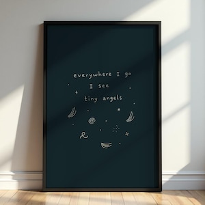 May include: A framed art print with a dark teal background and white text that reads "everywhere I go I see tiny angels." The print includes small, whimsical illustrations of stars, moons, and other celestial shapes.