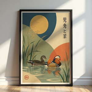 May include: Framed art print featuring two mandarin ducks swimming in water. The artwork has a Japanese aesthetic, with a large yellow sun, blue and orange geometric shapes, and tall green reeds. The print includes Japanese text and a red circular seal.