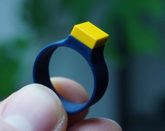 May include: A blue silicone ring with a yellow square on top.