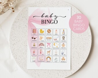 May include: A pink and white baby bingo card with 30 baby-themed squares. The squares include images of a book, rubber duck, baby's feet, bottle, castle, sunglasses, onesie, baby blocks, camera, teddy bear, stacking toy, rainbow, free space, moon and stars, sippy cup, baby, doll, cradle, mobile, bag, diaper, rocking horse, wall decor, clouds, and ABC blocks.