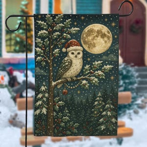 May include: A garden flag featuring a whimsical winter scene. An owl wearing a Santa hat perches on a snow-covered branch, with a full moon in the background. The flag is decorated with holly and Christmas tree imagery.