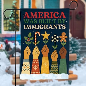 Könnte beinhalten: Eine marineblaue Gartenflagge mit dem Text "AMERICA WAS BUILT BY IMMIGRANTS". Die Flagge zeigt Illustrationen von Händen, die Feiertagssymbole wie Stechpalmen, eine Zuckerstange, einen Stern, eine Schneeflocke und einen Lebkuchenmann halten.