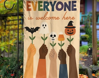 May include: A beige Halloween garden flag with the text "EVERYONE is welcome here." The flag features illustrations of hands holding up Halloween-themed flowers, including a bat, ghost, skull, and jack-o'-lantern.