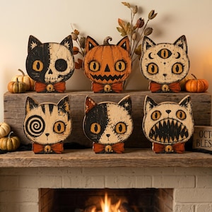 Peut inclure: Six plaques décoratives en bois en forme de chat avec diverses illustrations dont un crâne, une citrouille, un troisième œil, une spirale, des points de suture et des dents pointues. Chaque chat porte un nœud papillon rouge avec une clochette.